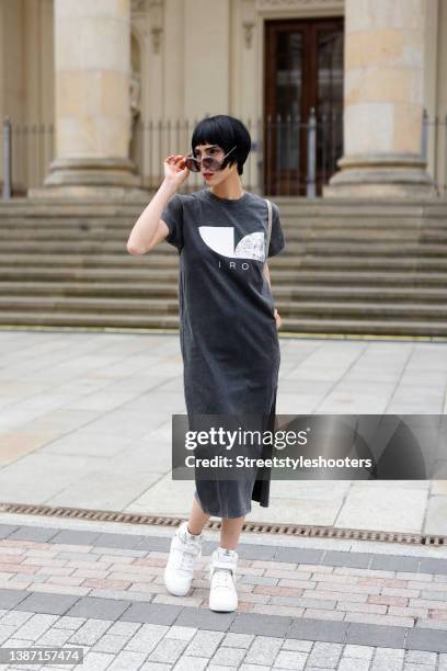 Model and artist Zoe Helali wearing a dark grey t-shirt dress with tigh high slit by Iro, sunglasses by Hies Optik, a beige bag by Balenciaga and...