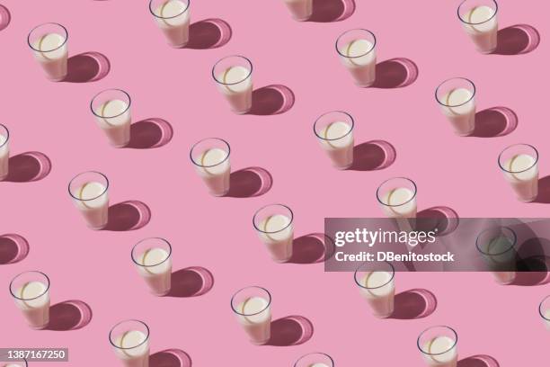 pattern of glass cups filled with milk in hard light on pink background. dairy, shortage, calcium, grow and drink concept - protein shake stock-fotos und bilder