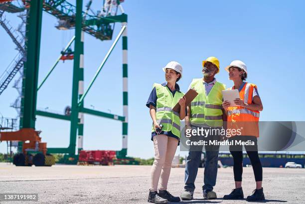 foreman engineer and dock workers holding digital tablet and clipboard looking at crane - shipyard crane stock pictures, royalty-free photos & images