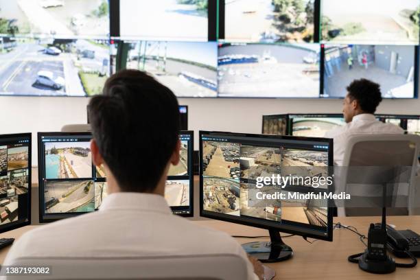 guardias de seguridad que trabajan en la sala de control mientras miran la pared de video - pared de vídeo fotografías e imágenes de stock