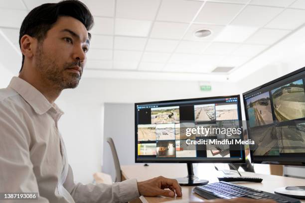 asian american security guard checking on monitors while sitting in control room - multiple screens stock pictures, royalty-free photos & images