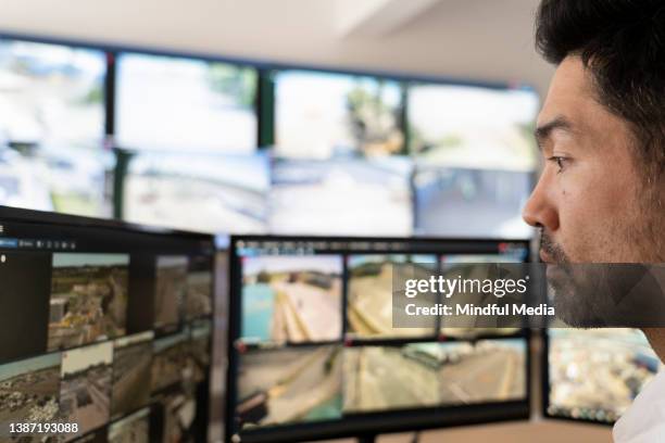 concentrated asian american male security guard watching monitors at control room - multiple screens stock pictures, royalty-free photos & images