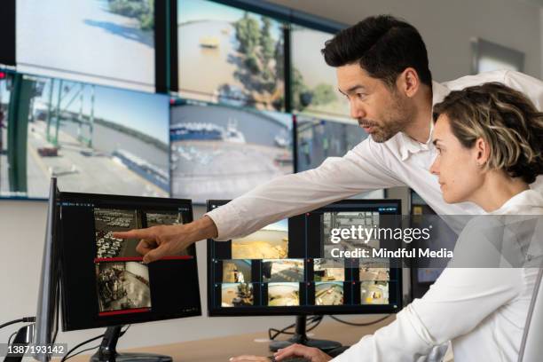 asian american male security guard pointing at monitor while discussing with female coworker - multiple screens stock pictures, royalty-free photos & images