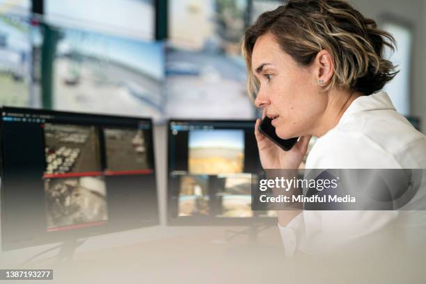 adult female engineer in shipyard control room using smart phone - multiple screens stockfoto's en -beelden