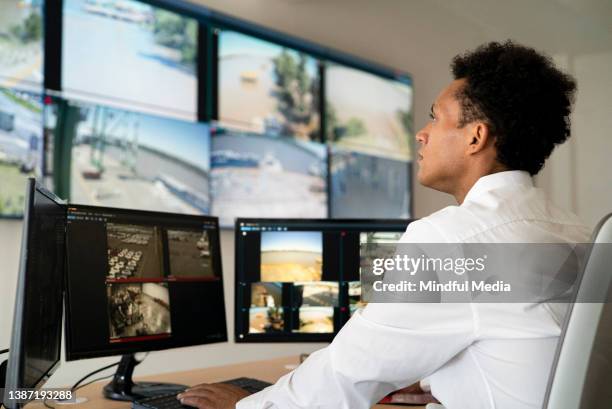 junge erwachsene männliche sicherheitsarbeiter, die videowand beobachten, während sie am schreibtisch sitzen - monitor wall stock-fotos und bilder