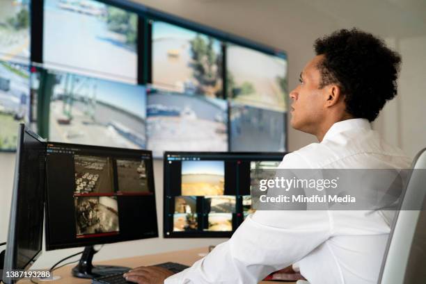 trabajador de seguridad masculino adulto joven viendo video wall mientras está sentado en el escritorio - surveillance fotografías e imágenes de stock