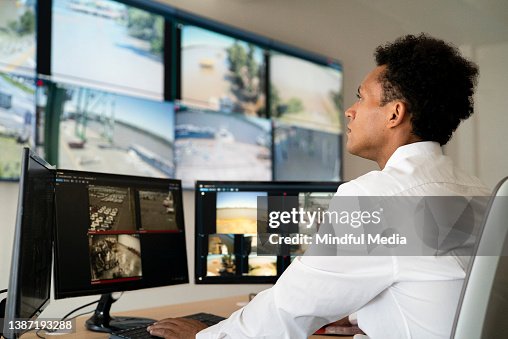 Young adult male security worker watching video wall while sitting at desk Young adult male security worker watching video wall while sitting at desk