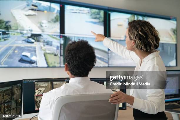 female and male security coworkers discussing while looking at video wall - bewakingscamera stockfoto's en -beelden