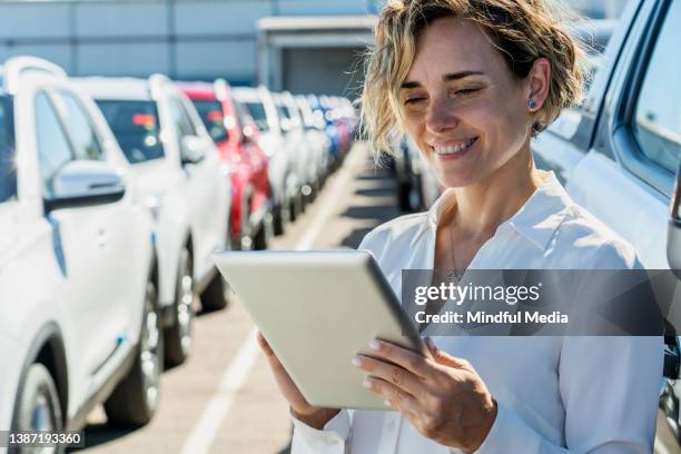 smiling saleswoman using digital tablet at car dealership - showroom stock pictures, royalty-free photos & images