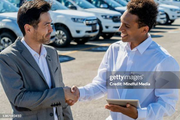 young car salesman shaking hand with businessman after a sale - car sale stockfoto's en -beelden
