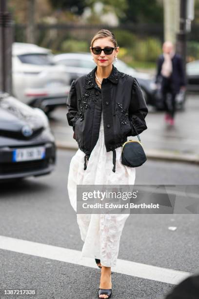 Jenny Walton wears black sunglasses, white pendant pearl earrings, a white pearls necklace, a white lace print pattern heart-neck / tank-top /midi...