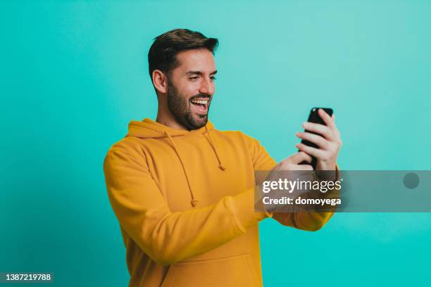 smiling man having a video call on a smartphone - hooded top stock pictures, royalty-free photos & images