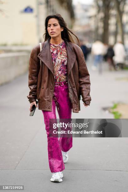 Nina Urgell Cloquell wears a beige with purple / black / pale yellow / dark brown print pattern t-shirt, a dark brown shiny leather oversized jacket,...