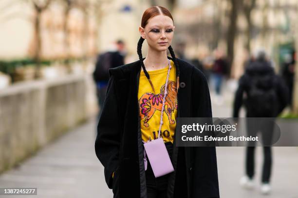 Sara Grace Wallerstedt wears black silk ribbons in the hair, a yellow with orange and pink tiger print pattern wool pullover, a black long coat, a...