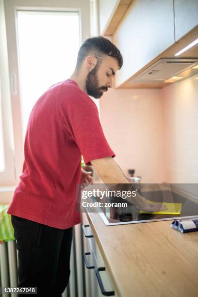 bearded young man cleaning glass-ceramic stove top at home - burner stove top 個照片及圖片檔