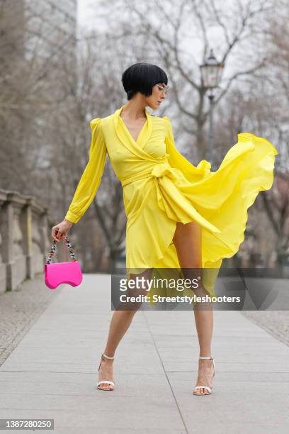Model and artist Zoe Helali wearing a yellow wrap midi dress by Viola Ballin, white vintage sandals, glasses by Hies Optik and a pink bag with...