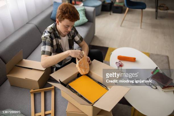 caring redhead teenage boy, a volunteer, packing the school supplies into cardboard box for donation - clear donation box stock pictures, royalty-free photos & images