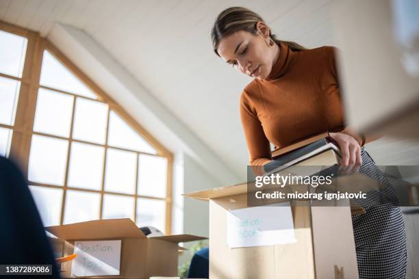 fürsorgliche kaukasische junge frau, die spielzeug und bücher zur spende in pappkarton verpackt - entrümpeln stock-fotos und bilder