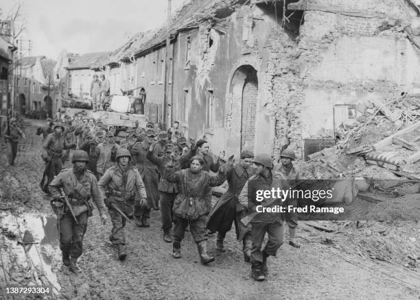 German soldier prisoners of war from the 340th Volksgrenadier Division with their arms raised above their heads walk into captivity through the shell...
