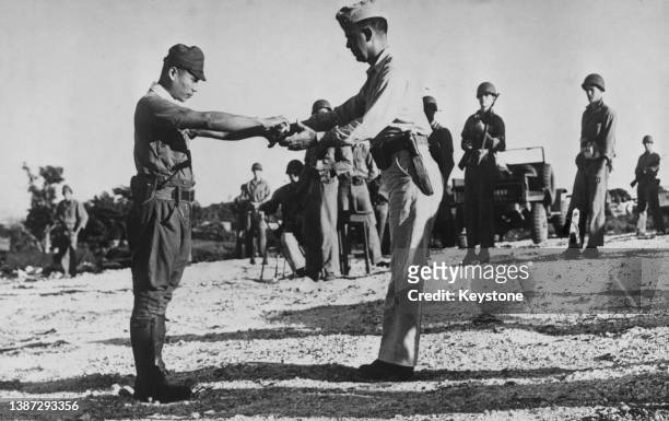 Captain Sakae Oba of the 18th Infantry Regiment, 31st Army of the Imperial Japanese Army surrenders his samurai sword to Lieutenant Colonel Howard G...