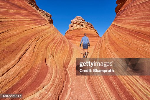 Hiker Exploring The Famous Wave of Coyote Buttes North in the Paria Canyon-Vermilion Cliffs Wilderness of the Colorado Plateau in Southern Utah and Northern Arizona USA Hiker Exploring The Famous Wave of Coyote Buttes North in the Paria Canyon-Vermilion Cliffs Wilderness of the Colorado Plateau in Southern Utah and Northern Arizona USA