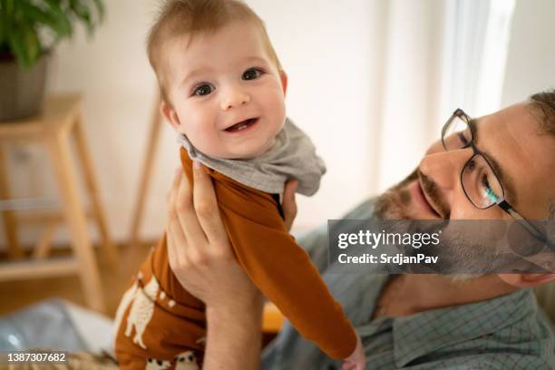 curious baby boy looking at camera, while his father holding him - baby bib stock pictures, royalty-free photos & images