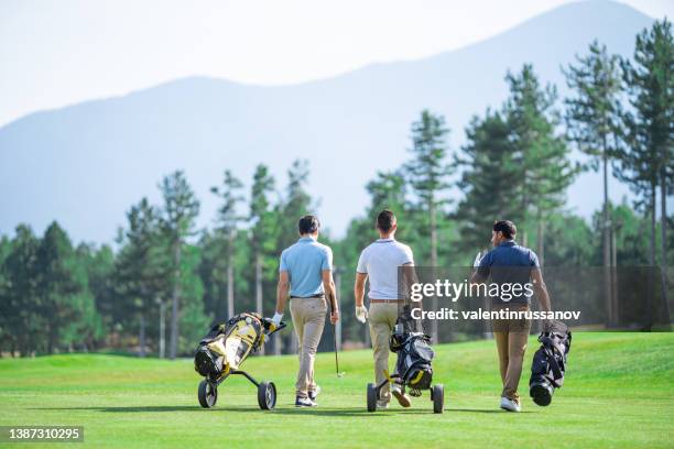 vista trasera de tres amigos golfistas masculinos, jugando al golf en un hermoso día soleado, caminando por el campo de golf con su equipo de golf - golf club fotografías e imágenes de stock