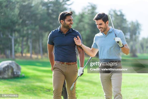 smiling young golf players holding their golf clubs on the golf course, walking, discussing and laughing - billionaire stock pictures, royalty-free photos & images