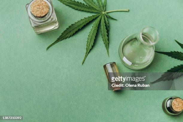 green cannabis leaves and cbd oil jars on green background. - cannabis oil - fotografias e filmes do acervo