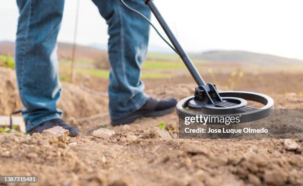 unrecognized person searching for objects with a metal detector in the countryside during a sunset, close up of search coil. - schatzoeken stockfoto's en -beelden