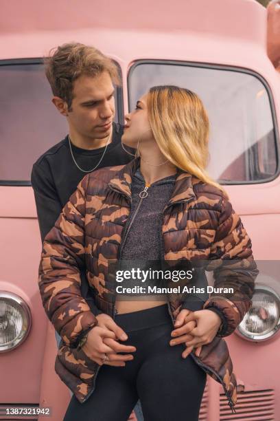 couple posing and gazing into each other's eyes in front of a pink van. - felicidad duran fotografías e imágenes de stock