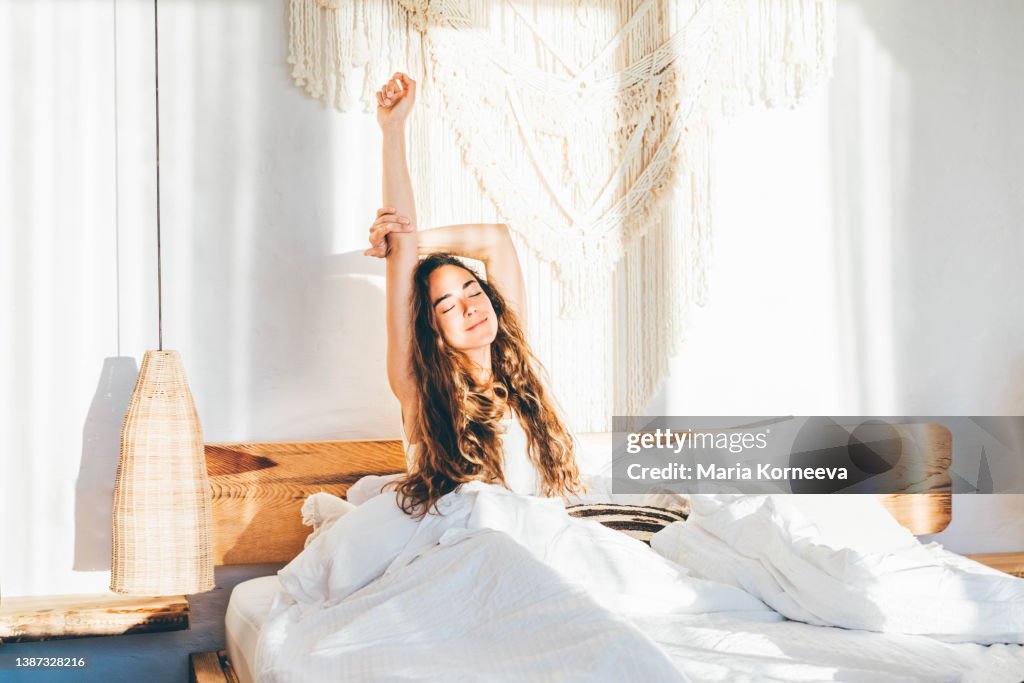 Woman relaxing on a bed. Woman stretching hands in bed.