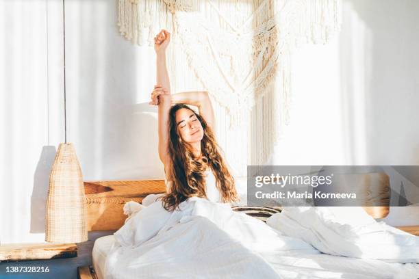 woman relaxing on a bed. woman stretching hands in bed. - wakker worden stockfoto's en -beelden