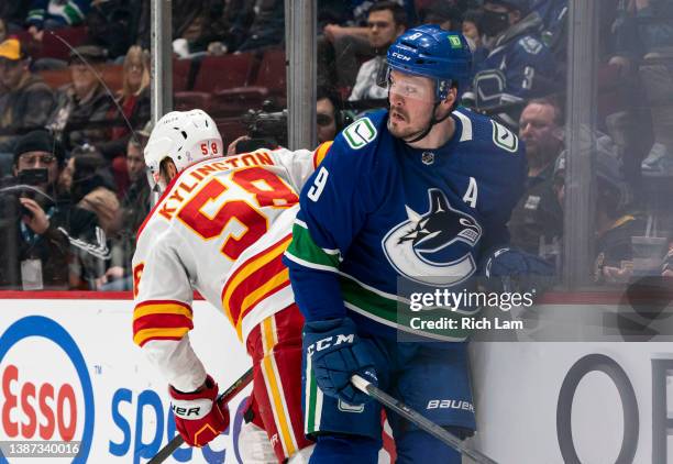 Miller of the Vancouver Canucks hits Oliver Kylington of the Calgary Flames along the end boards during NHL action on March 2022 at Rogers Arena in...