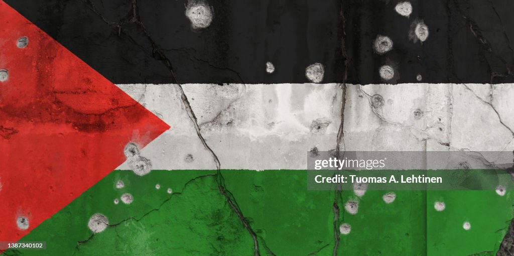 Full frame photo of a weathered flag of Palestine painted on a cracked wall with bullet holes.