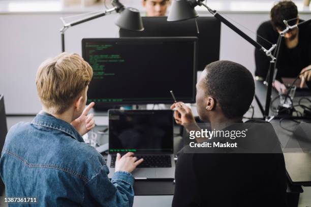 male computer programmers discussing over codes at desk in office - coderen stockfoto's en -beelden