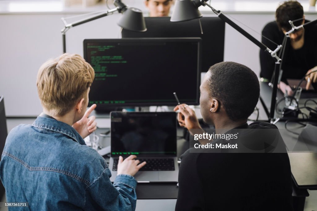 Male computer programmers discussing over codes at desk in office