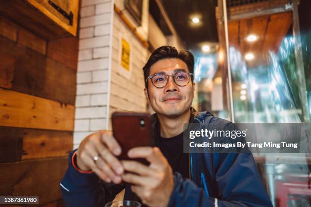 young handsome asian man using his smartphone joyfully in a restaurant - asian man texting ストックフォトと画像