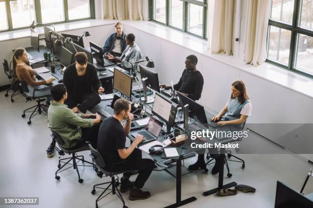 high angle view of male and female programmers working on computers at desk in office - arbeit und beschäftigung stock-fotos und bilder