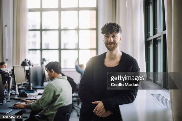 portrait of confident male computer leaning on window sill in office - incidental people stock pictures, royalty-free photos & images