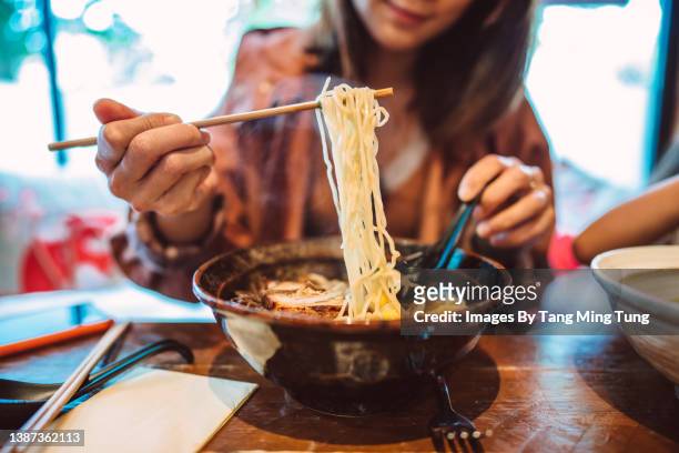 young asian woman enjoying japanese noodle soup in a japanese restaurant - chopsticks stock-fotos und bilder