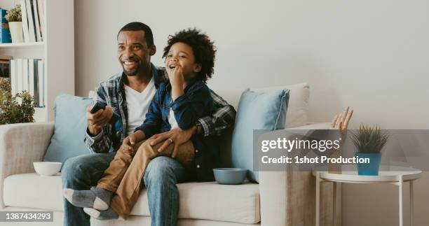 padre e figlio che guardano la tv a casa. cambio di canale. - african watching tv foto e immagini stock