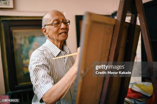 senior artist painting on canvas in his studio - indian old man stock-fotos und bilder