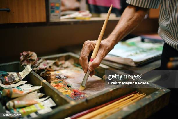 cropped hand of a senior artist with painting brush and wooden colour palette - artist painter stock-fotos und bilder