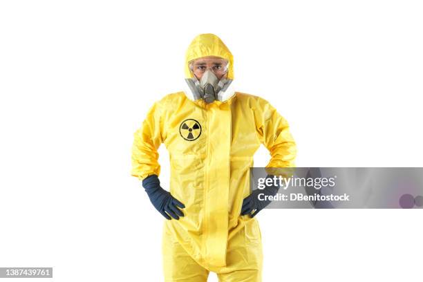 technician in yellow nuclear protection suit, mask and goggles, posing with arms akimbo, on white background. concept of nuclear energy and pandemics. - massenvernichtungswaffe stock-fotos und bilder