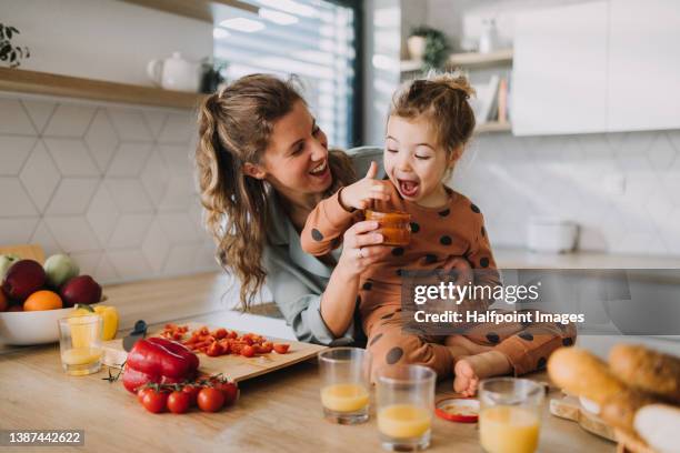 young mother feeding little daughter when preparing breakfast together in kitchen. - mother daughter kitchen stock-fotos und bilder