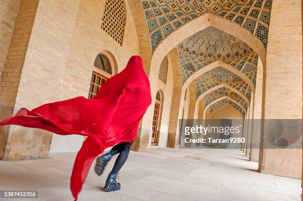 woman in red cloak running traditional iranian style courtyard - iran women stockfoto's en -beelden