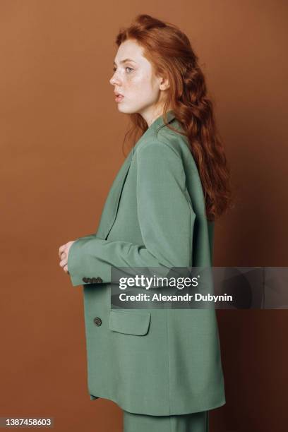 portrait in profile of a beautiful caucasian woman in a green suit on a brown colored background in a studio shot. fashionable girl model indoors in a new collection of clothes. - flerfärgad kostym bildbanksfoton och bilder