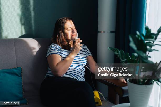 brown haired relaxed woman with close eyes, using nebulizer for inhalation, breathing problem disease. sitting on a couch near light window - medical oxygen equipment 個照片及圖片檔