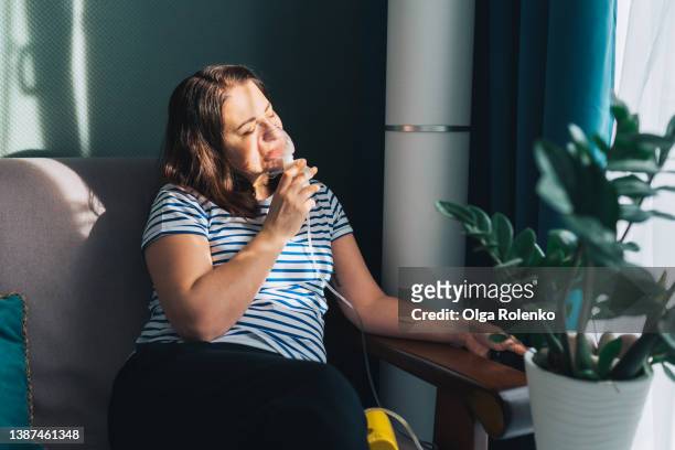 brown haired tranquil woman with close eyes, using nebulizer for inhalation at home, breathing problem disease. - breathing device stock pictures, royalty-free photos & images